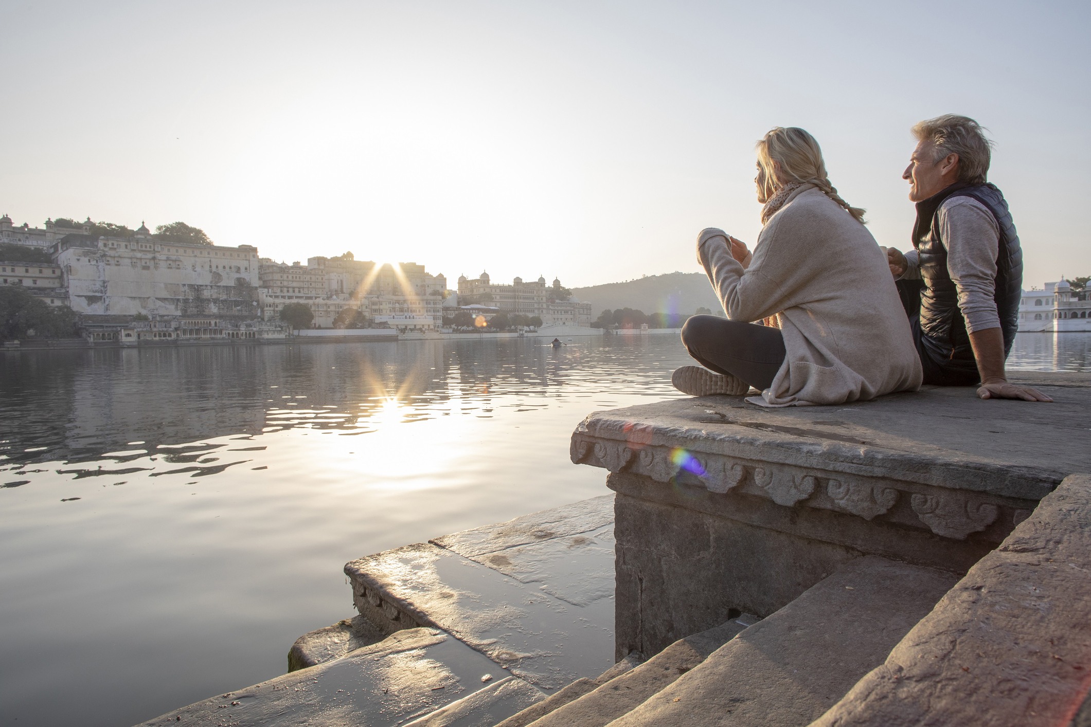Pareja sentada frente a un lago, disfrutando de un atardecer y representando la tranquilidad y libertad de la jubilación anticipada