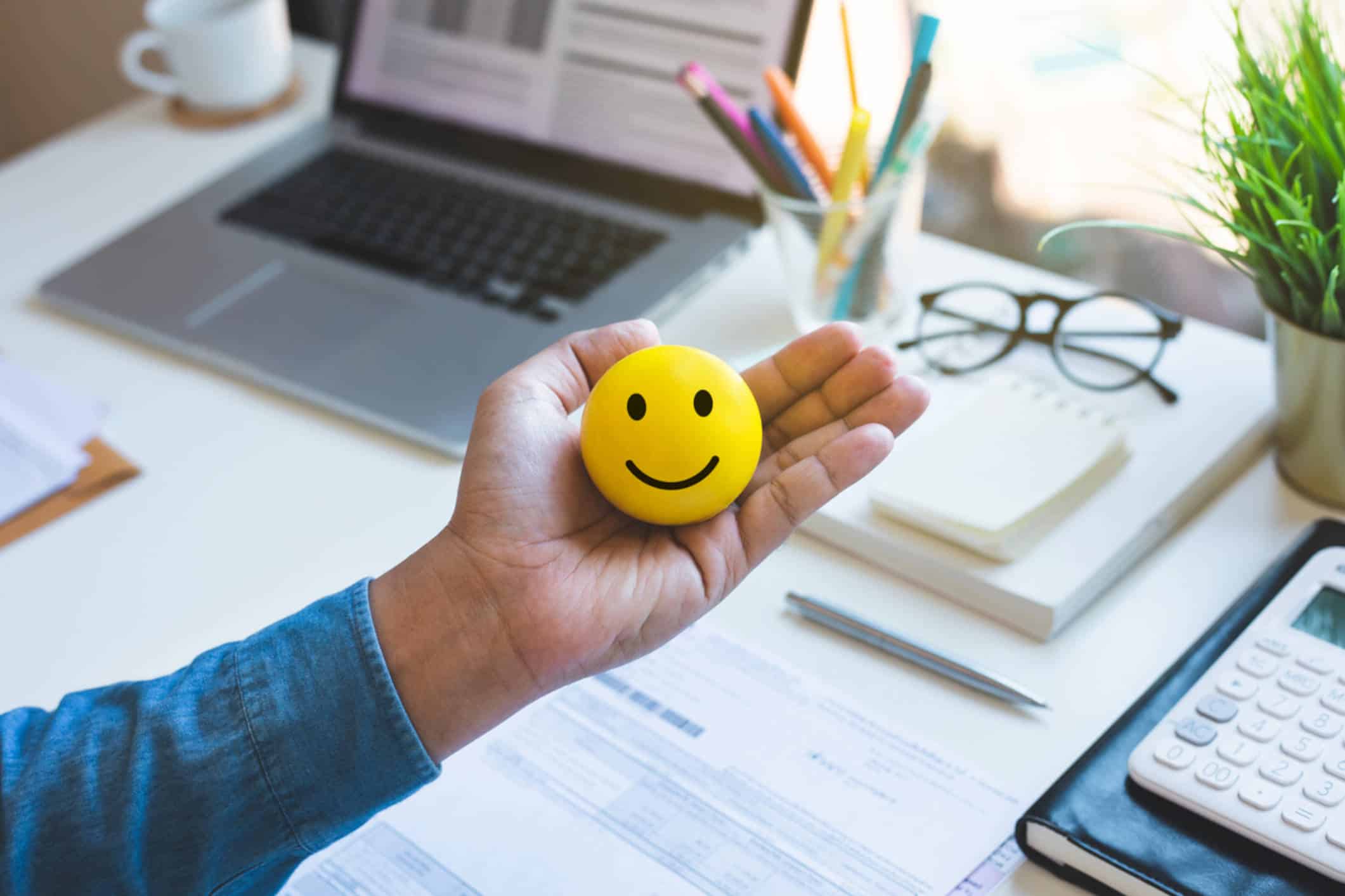 pelota amarilla con una cara sonriente en su escritorio, símbolo del bienestar y la salud mental en el trabajo.