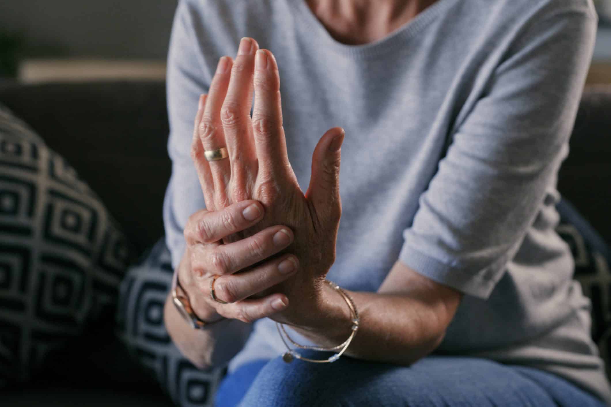 Mujer con las manos entrelazadas, con aparente molestia en las articulares, representando el cuidado de las articulaciones durante el invierno.