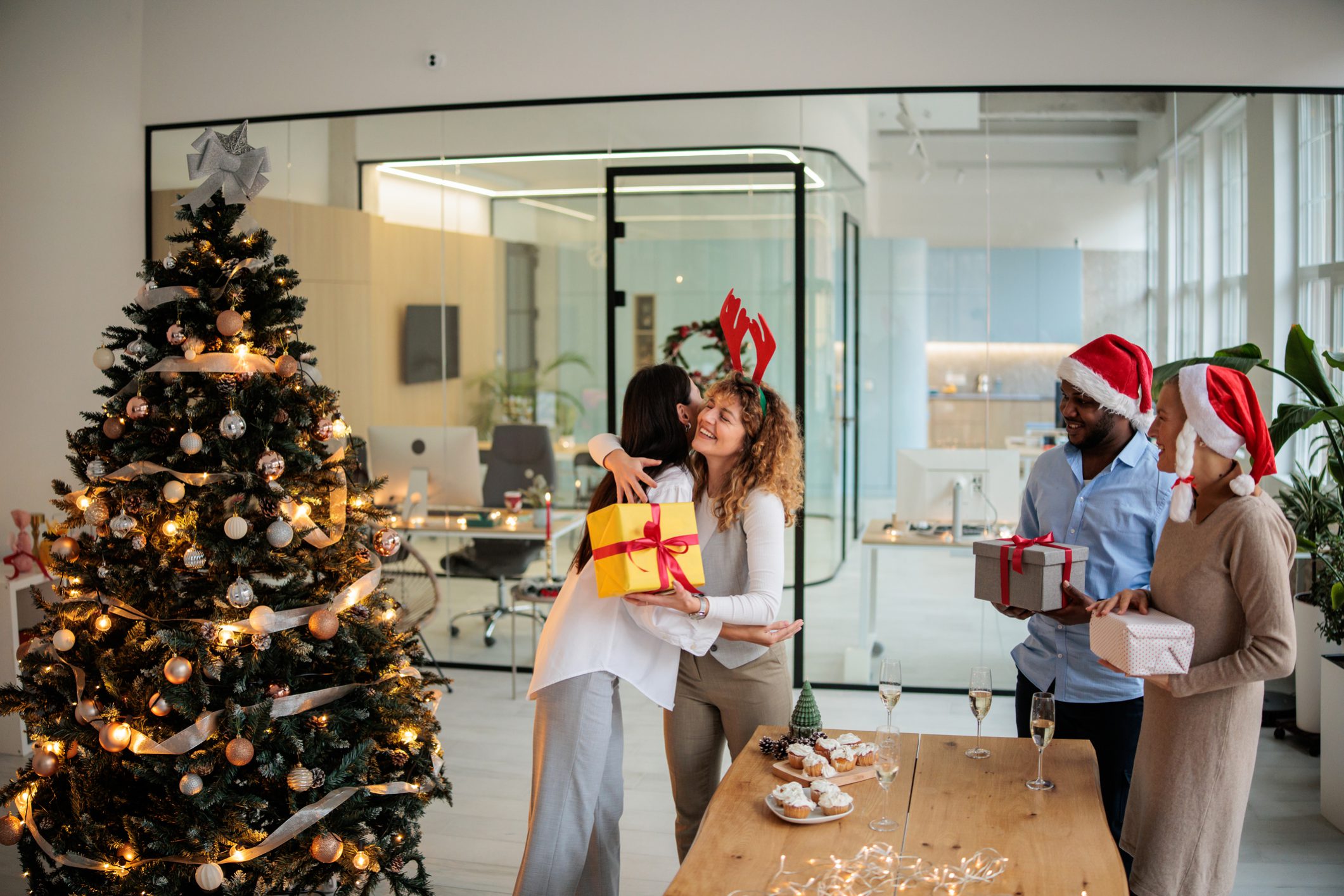 Empleados celebrando la Navidad en la oficina, intercambiando regalos junto al árbol.